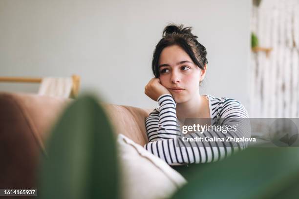 upset teenage girl looking away and sitting in room at home - 16 17 years stock pictures, royalty-free photos & images