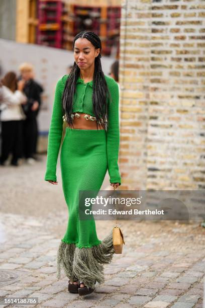 Guest wears a green braided wool shirt neck / long sleeves cropped jacket, a matching green braided wool high waist long fringed skirt, a beige matte...