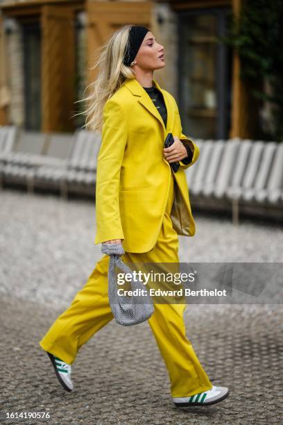 Guest wears a black large headband, a black t-shirt, a yellow oversized blazer jacket, yellow large suit pants, a gray satin with rhinestones mesh /...