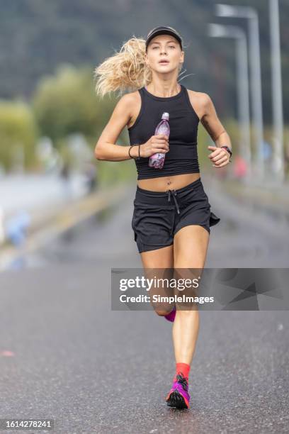 good looking woman runner running marathon with water bottle in hand. - joggeuse photos et images de collection