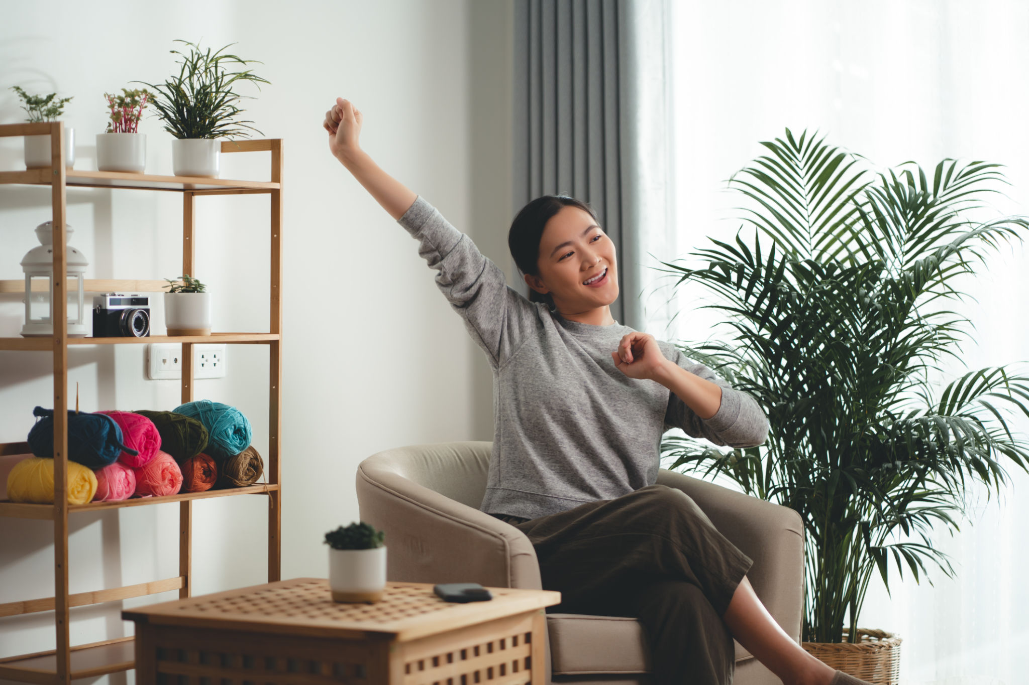 Asian woman sitting on armchair in living room relaxing stretching body breathing fresh air at home. Asian woman sitting on armchair in living room relaxing stretching body breathing fresh air at home.