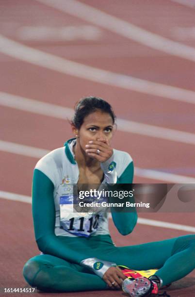 Australian athlete Cathy Freeman her hand over her mouth as she sits on the running track after winning the women's 400 metres event of the 2000...