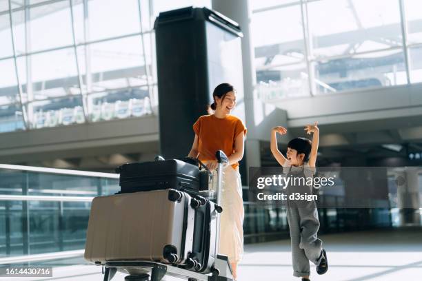 joyful young asian mother and little daughter travelling together, they are pushing a luggage trolley with suitcases at airport terminal. ready for a trip. travel and vacation concept - chariot photos et images de collection