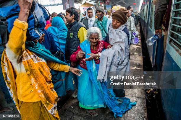An elderly lady is helped along the platform as Hindu devotees board their train at Allahabad train station, the site of last night's stampede,...