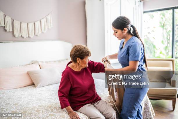 home caregiver assisting a senior woman to get clothed in a nursing home - seniorenhuis stockfoto's en -beelden