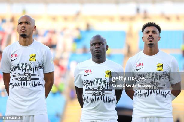 Fabinho, N'Golo Kante, and Ahmed Bamsaud of Al-Ittihad looks on as they line up prior to the Saudi Pro League match between Al Raed and Al-Ittihad at...