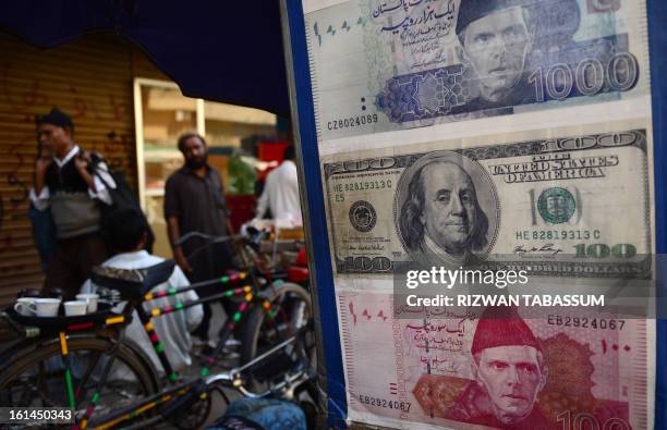 Pakistani pedestrians walk past a roadside currency exchange stall displaying examples of Pakistani and US currency notes in Karachi on February 11,...