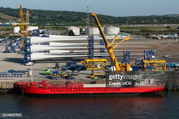 Belfast, Northern Ireland, UK, Red ship with open hatches and a crane unloading turbine blades and equipment relating to wind energy for assembling.