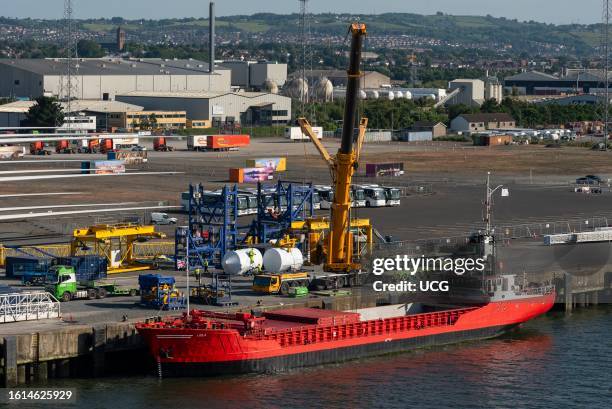 Belfast, Northern Ireland, UK, Red ship with open hatches and a crane unloading turbine blades and equipment relating to wind energy for assembling.