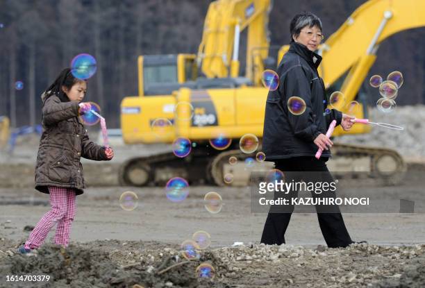 Hiroko Oyama and her granddaughter play with bubbles as they pray for victims of the 74 elementary school children at the Okawa elementary school as...