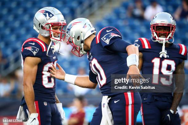 Mac Jones of the New England Patriots high fives teammate Tre Nixon as Isaiah Zuber smiles prior to an NFL preseason game against the Washington...