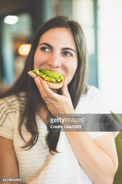 millenial woman eats an open faced avocado toast sandwich - avocado toast stock pictures, royalty-free photos & images