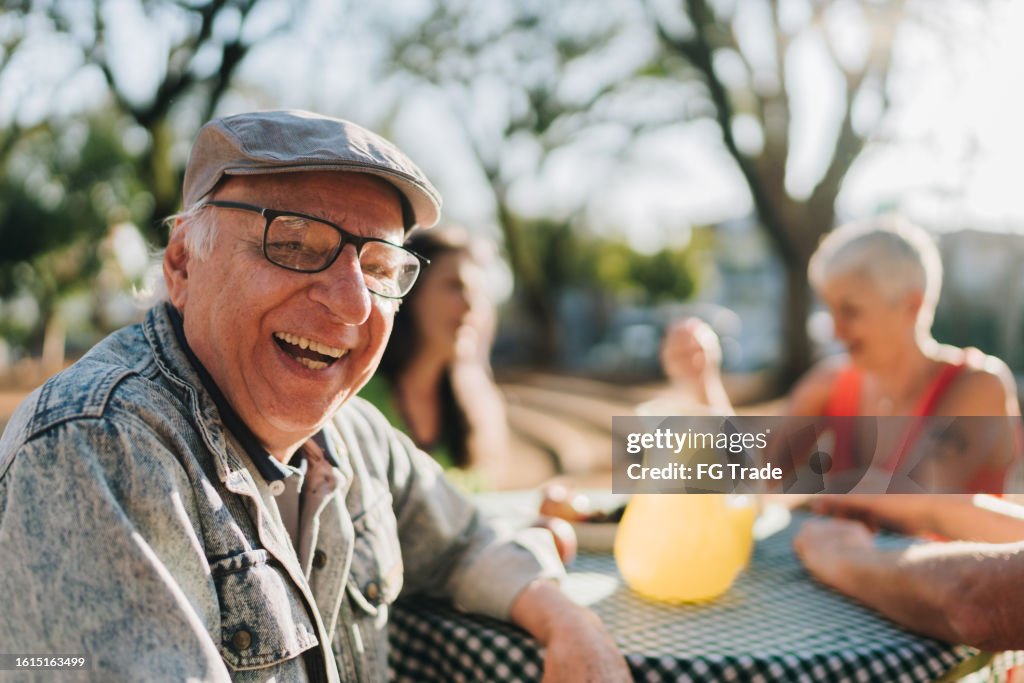 Portrait of a senior man with friends during picnic in a public park