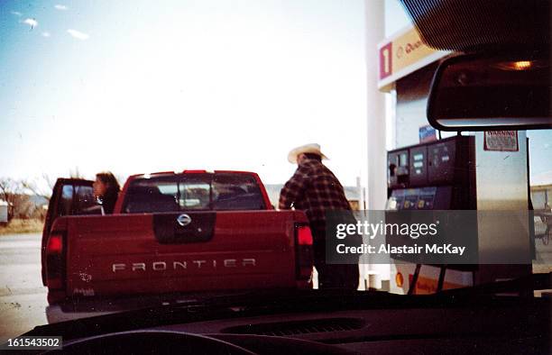 Man in a cowboy hat stops to fuel his pick-up truck at a gas staion in West Texas .
