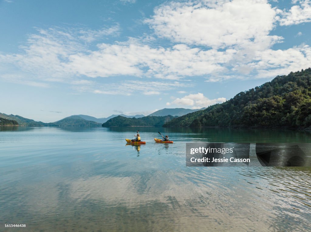 Drone shot of two people canoeing side by side on remote lake with hill surrounds