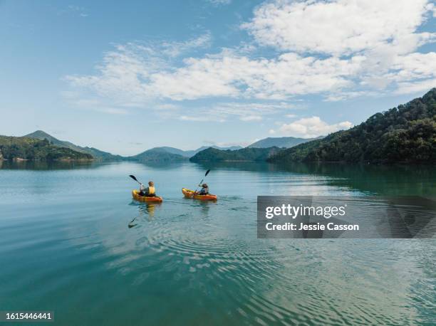 drone shot of two people canoeing side by side on remote lake with hill surrounds - kajakdisziplin stock-fotos und bilder