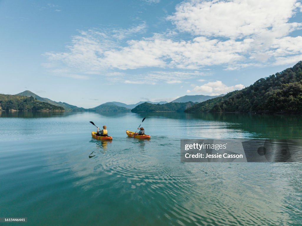 Drone shot of two people canoeing side by side on remote lake with hill surrounds