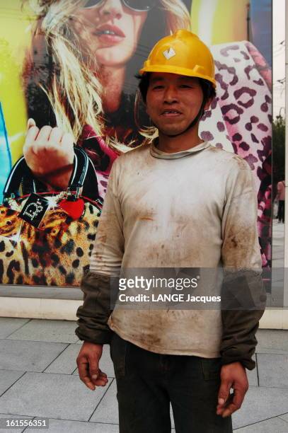 Shanghai The Traditional. Ouvrier chinois en tenue de travail et casque de chantier jaune posant devant un grand panneau publicitaire dans une rue de...