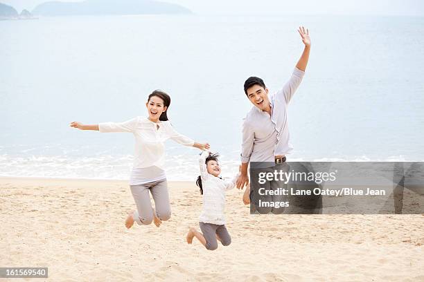 excited young family jumping in mid-air on the beach of repulse bay, hong kong - hong kong family stockfoto's en -beelden