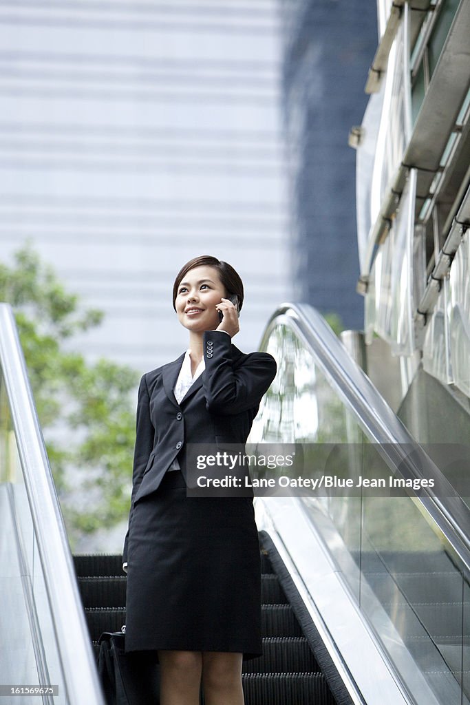 Young businesswoman standing on escalator and talking on the phone, Hong Kong