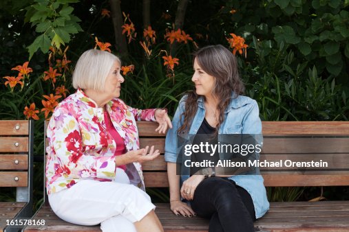 Mother and daughter talking on park bench Mother and daughter talking on park bench