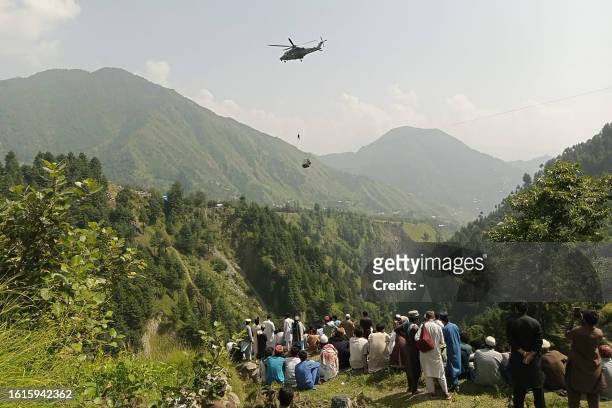 People watch as an army soldier slings down from a helicopter during a rescue mission to recover students stuck in a chairlift in Pashto village of...