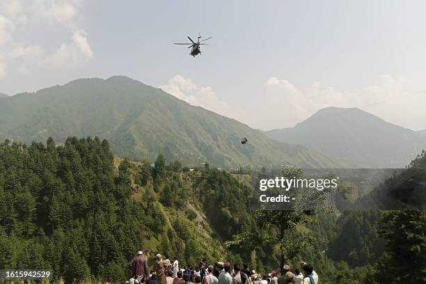 People watch as an army helicopter conducts a rescue mission to recover students stuck in a chairlift in Pashto village of mountainous Khyber...