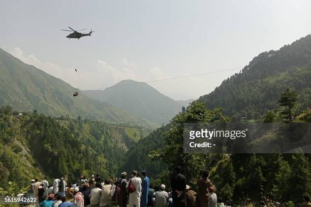People watch as an army soldier slings down from a helicopter during a rescue mission to recover students stuck in a chairlift in Pashto village of...
