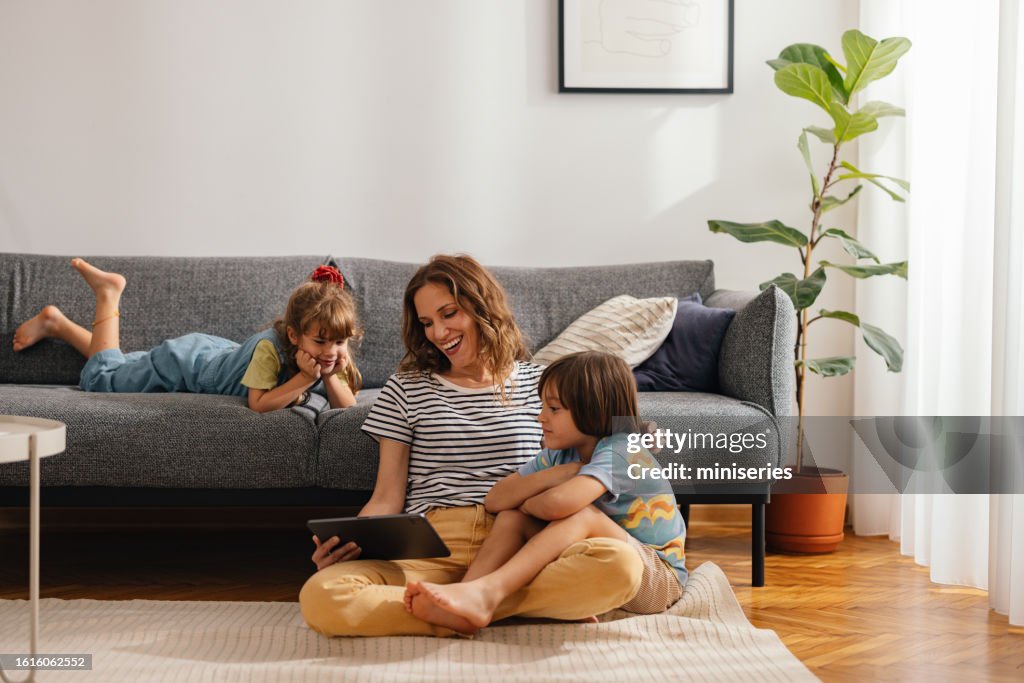 Momentos felizes em família: a mãe senta-se no chão e assiste a algo no tablet digital com os filhos
