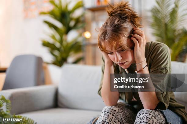 giovane donna triste seduta sul divano di casa - one young woman only foto e immagini stock