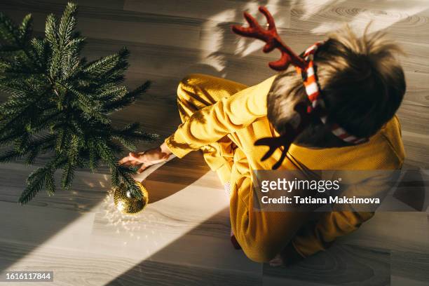little boy in yellow pajama decorates the christmas tree with a glitter ball. - golden boy stock pictures, royalty-free photos & images