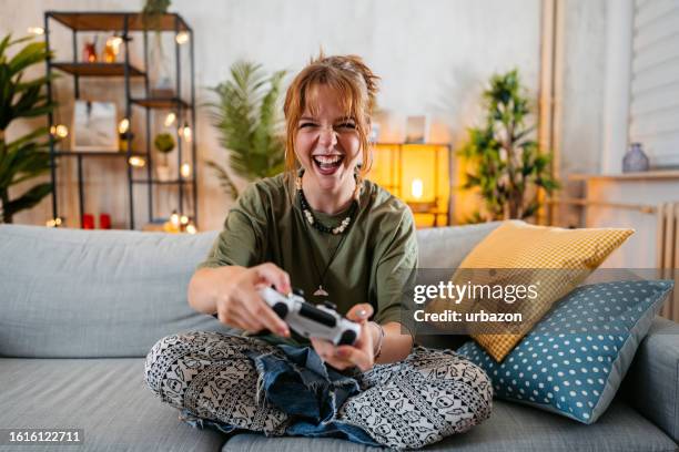 mujer joven jugando videojuegos en casa - videojuegos fotografías e imágenes de stock