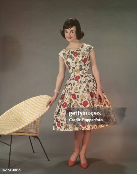 Posed studio portrait of a female fashion model wearing a floral patterned sleeveless summer dress with full skirt, London, 7th May 1960.