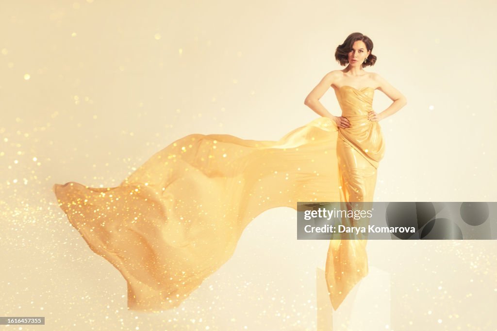 A beautiful full-length woman on the podium in a gold flowing long dress with gold particles. The concept of awards, victories, ceremonies with the black tie dress code.