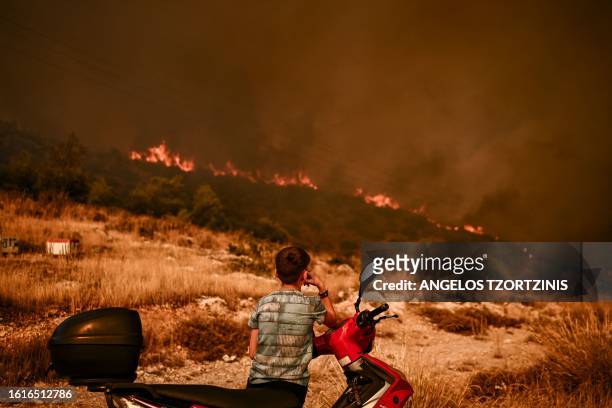 Young boy looks at a wildfire in Chasia in the outskirts of Athens on August 22, 2023. Greece's fire brigade on August 22, 2023 ordered the...