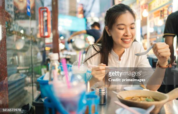 young cheerful asia women eating chinese food style noodles in a streetfood marketplace in chinatown - singapore food stockfoto's en -beelden