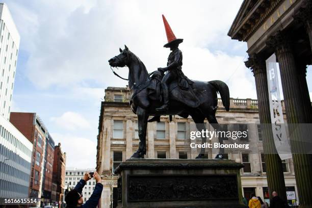 Tourist takes a photograph of the Duke of Wellington statue crowned with a traffic cone outside the Gallery of Modern Art in the center of Glasgow,...