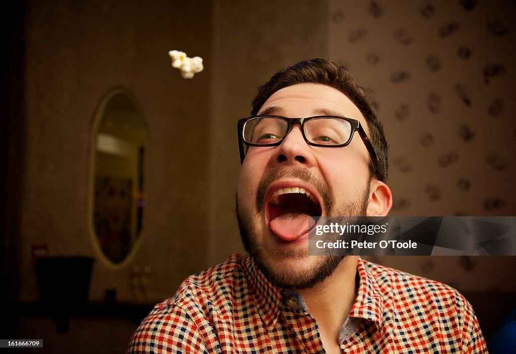 Popcorn thrown into mouth of a young bearded man