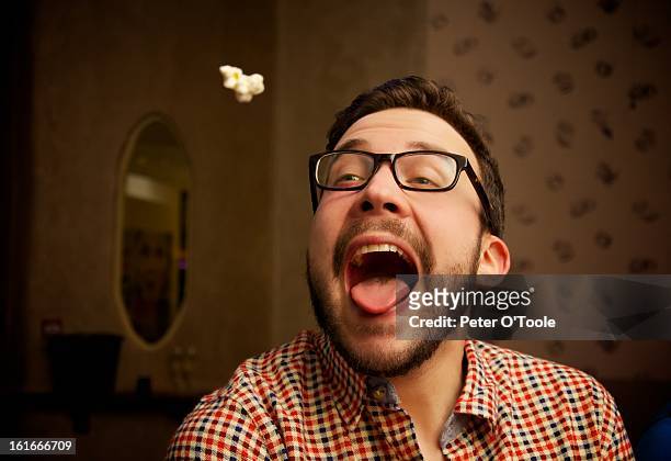 popcorn thrown into mouth of a young bearded man - throwing stock pictures, royalty-free photos & images