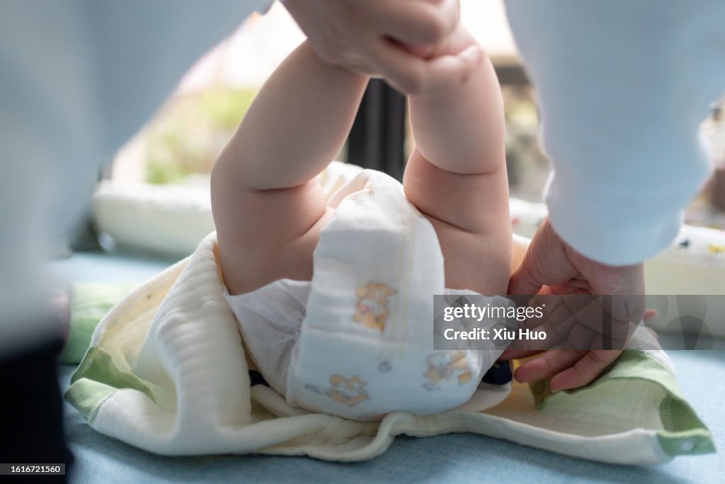An Asian mother is changing her baby's diapers