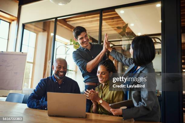 diverse group of entrepreneurs cheering and laughing at video presentation on laptop in boardroom - high five stockfoto's en -beelden