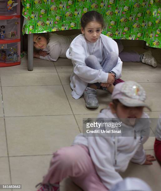 A girl hides under a table as Israeli schoolchildren take cover in a bomb shelter during a Home Front command drill simulating a rocket hitting a...