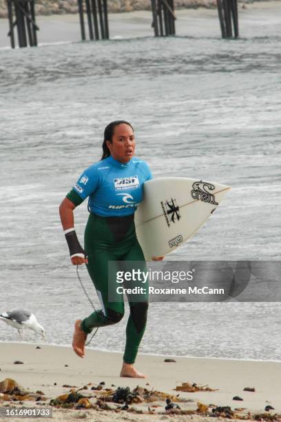 Hawaiian surfer Melanie Bartels runs up the beach with a Kazuma surfboard and a wrapped right wrist with the Malibu Pier in the background and a...