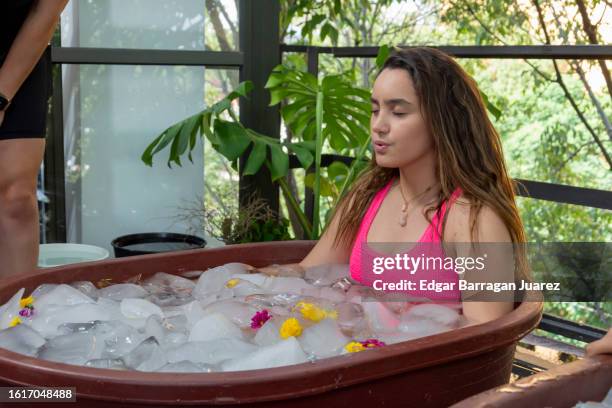 woman with pink bikini inside a tub with ice practicing cryotherapy - bad breath stockfoto's en -beelden