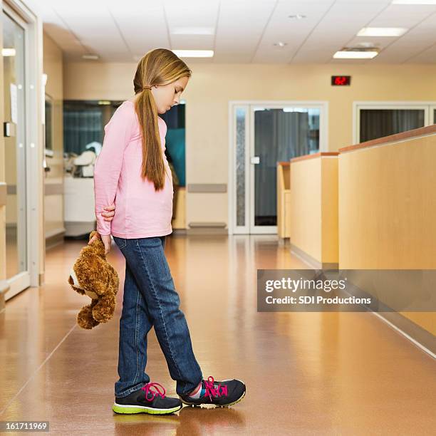 sad little girl holding teddy bear in hospital hallway - sad child hospital stock pictures, royalty-free photos & images