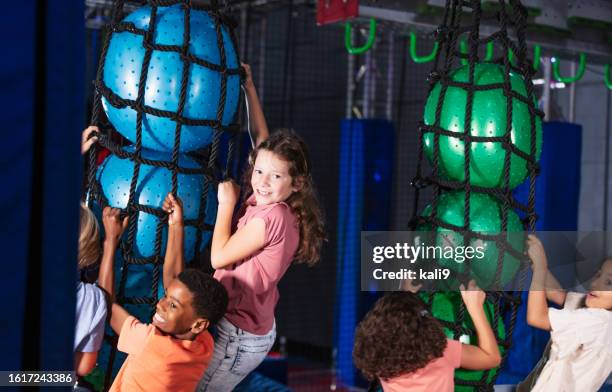 girl with friends climbing at indoor amusement park - netting stock pictures, royalty-free photos & images