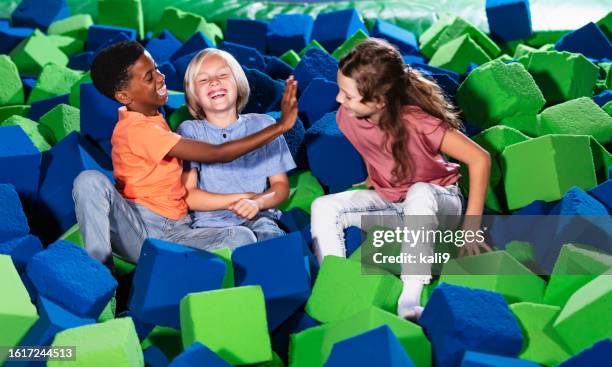 three multiracial children play in pool of foam blocks - ball pit stock pictures, royalty-free photos & images