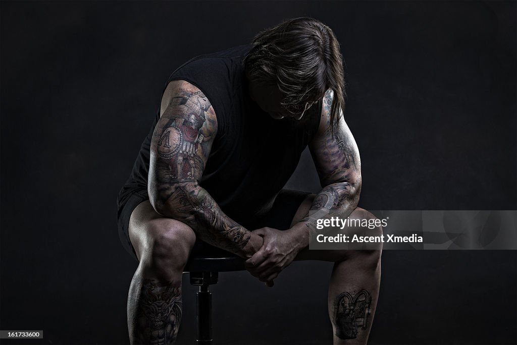 Man with multiple tattoos sits in dark,illuminated