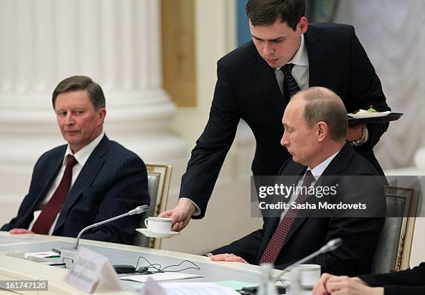 Russian President Vladimir Putin receives a cup as Head of the Presidential Administration Sergey Ivanov looks on during a meeting with G20 finance...