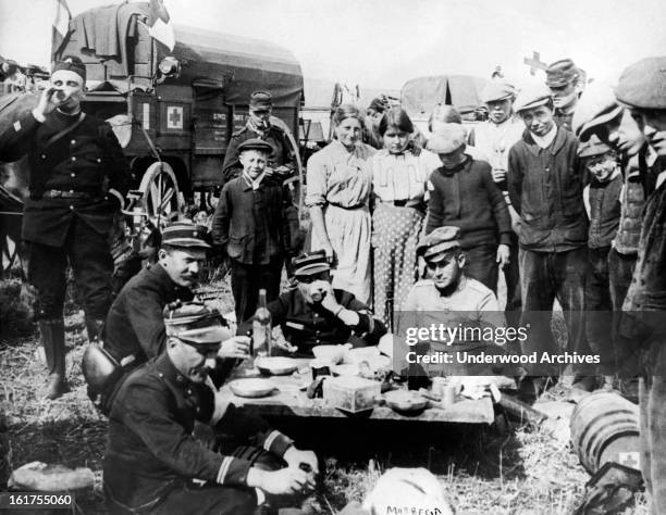 French officers of an ambulance division dine by the side of the road with a German Red Cross prisoner who has fallen into their hands, Argonne...